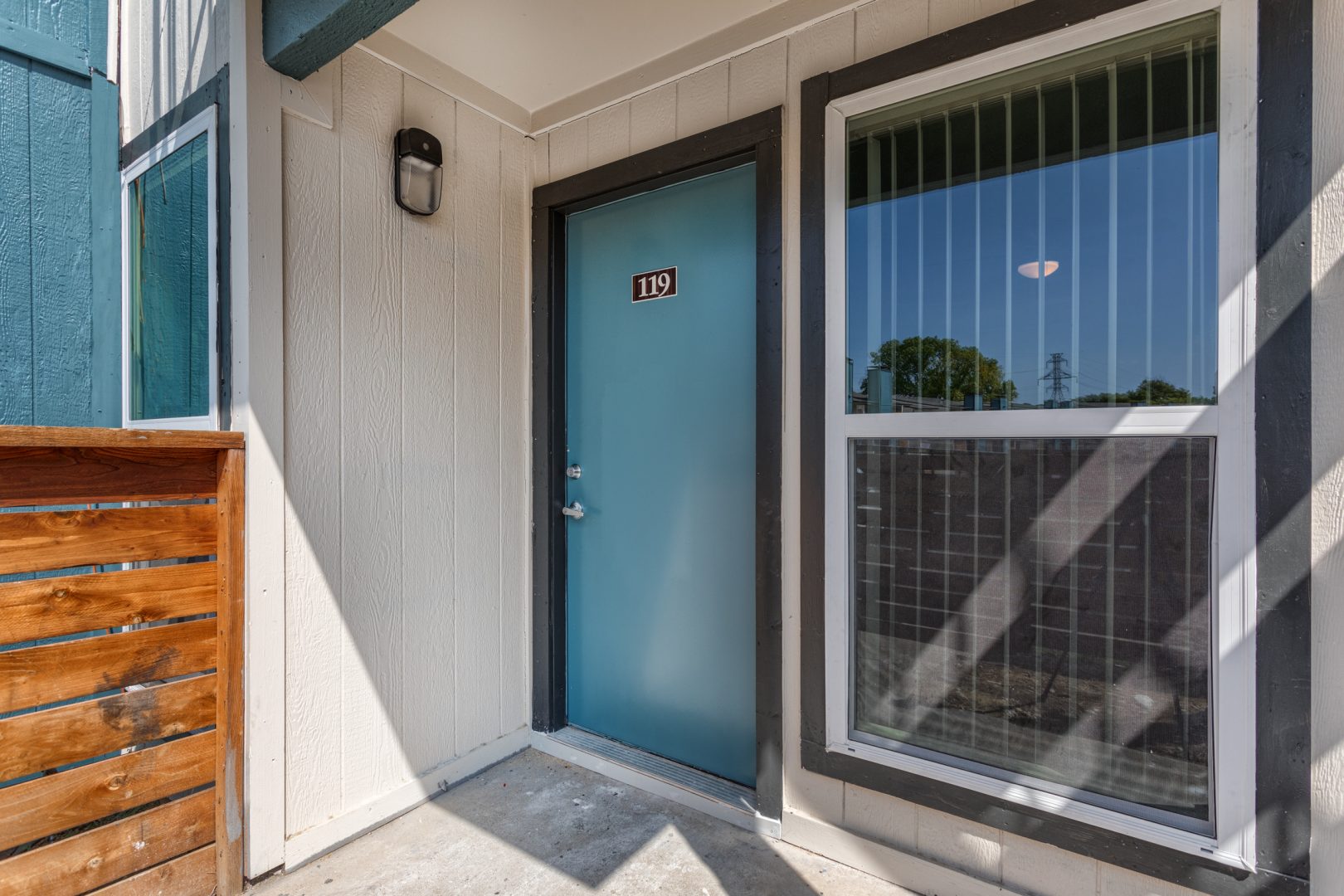 Picture of a blue apartment entryway door and window with a small section of cedar fence showing.