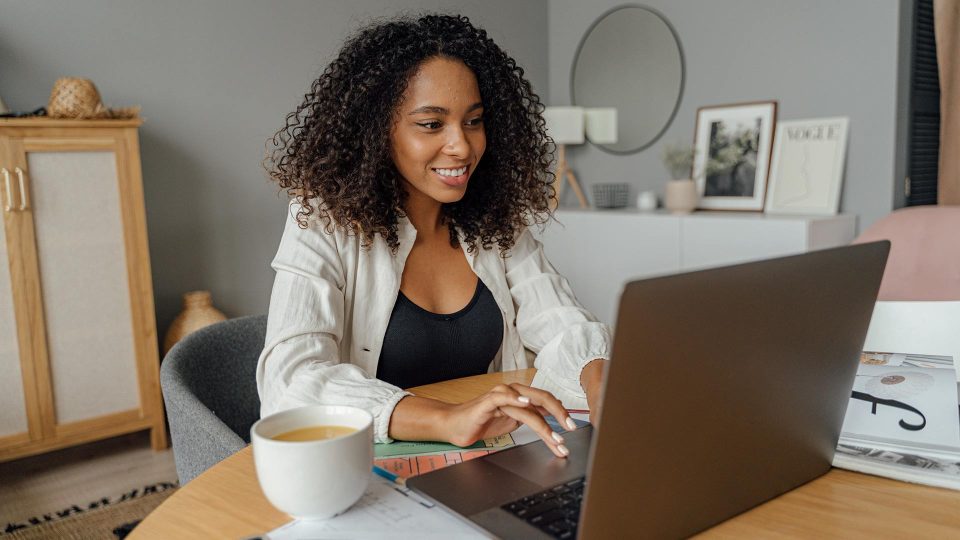 twenty something female sitting at a table with a cup of coffee and a laptop