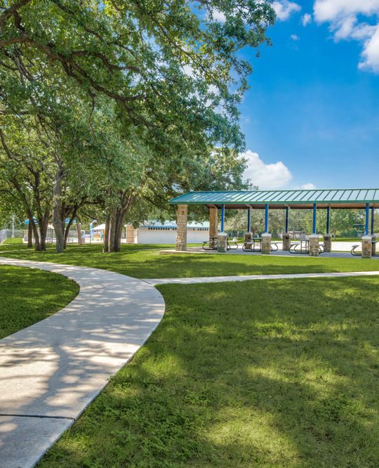 Picture of a green space with a sidewalk and a covered picnic area.
