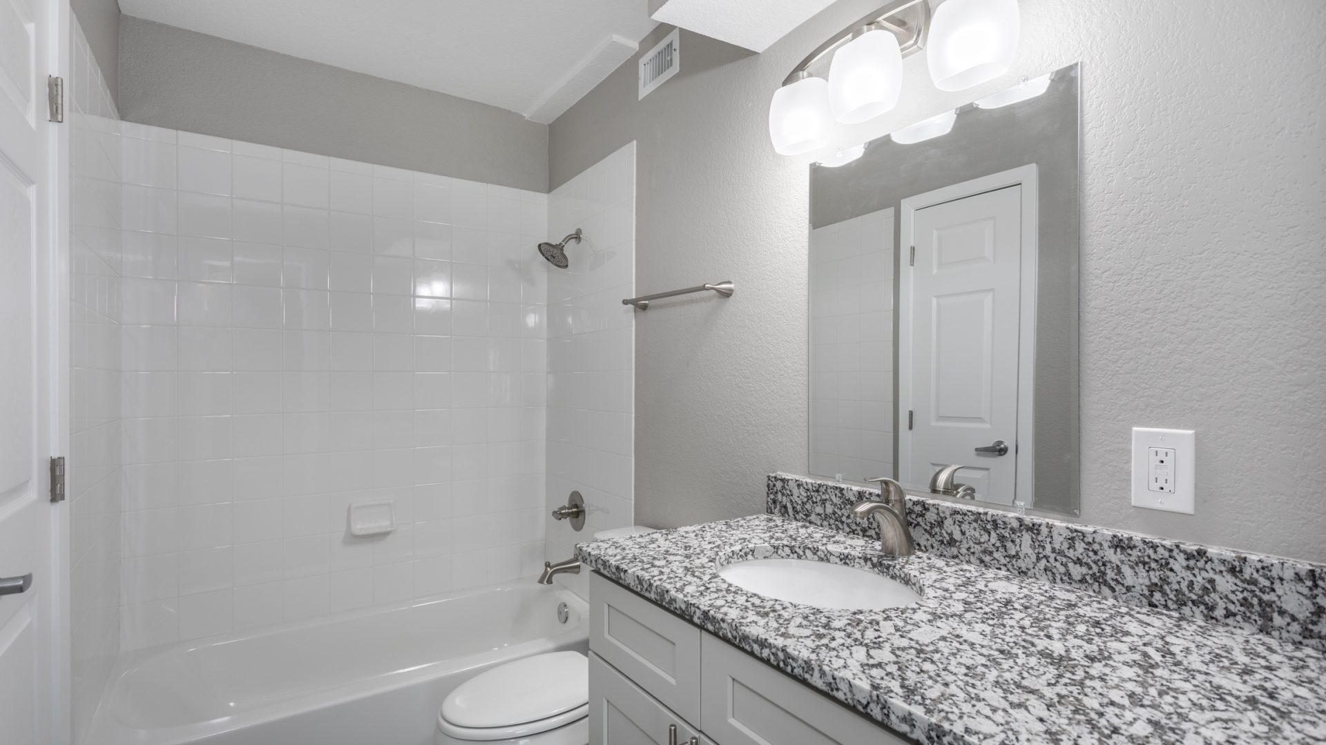 Picture of a bathroom with light gray walls, black and white granite countertops, and a white shower/toilet.